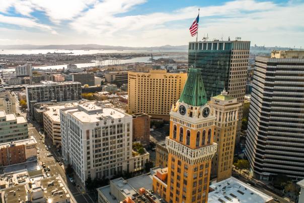 Aerial view of downtown Oakland cityscape with the iconic Tribune Tower, modern skyscrapers, and waterfront.