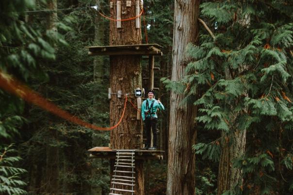 A person getting ready to cross an uneven and tipsy wooden bridge on a high ropes course.