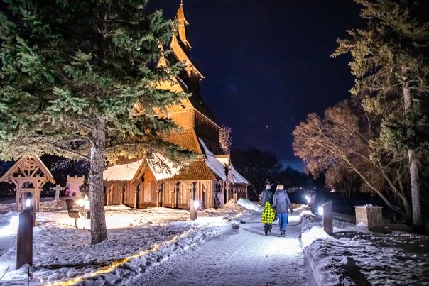 People walking the trail along the stave church at night in winter.