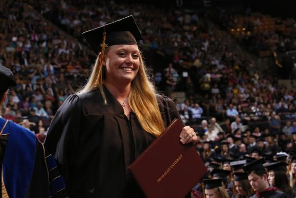 A young woman smiles at the camera with her diploma at Texas State University graduation in San Marcos, Texas