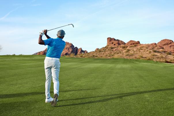 Man playing golf at Papago Golf Course with scenic desert landscape in the background, mid-swing on the green