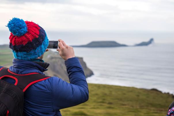 A person in a bobble hat taking a photo of Worm's Head