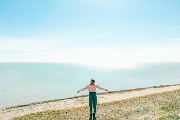 woman with arms out in front of water