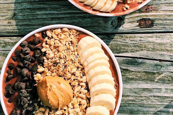 Two smoothie bowls filled with sliced bananas, oats, chocolate chips and peanut butter