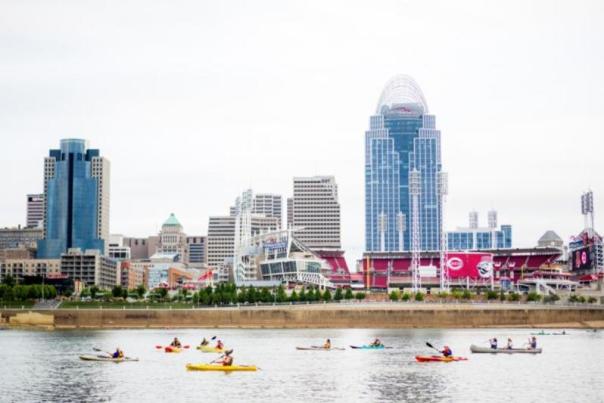 Image is of people kayaking along the Ohio River with the City of Cincinnati in the background.
