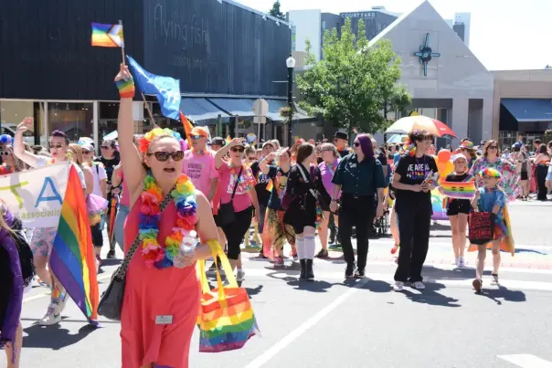 A person in rainbow and hot pink carrying a pride flag in a pride parade.