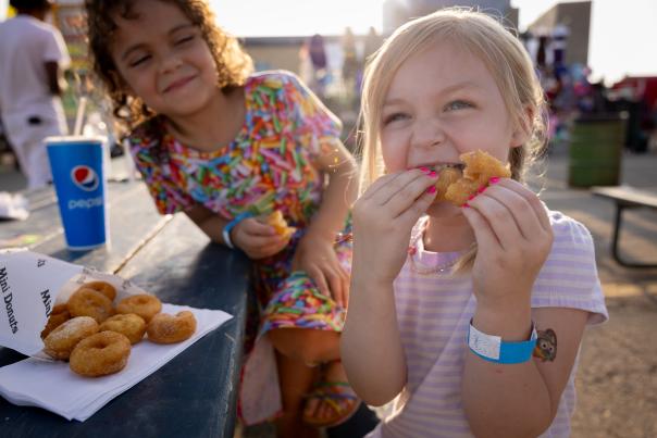 Two young girls eating miniature donuts at a pumpkin patch