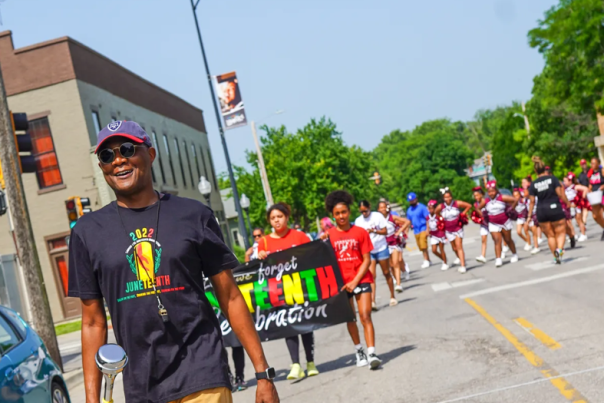 Photo taken at the Lawrence Juneteenth parade which features a man smiling in the foreground and cheerleaders in the background.