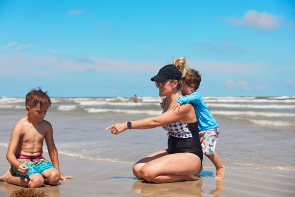 Mom and sons on the beach sitting in shallow water.