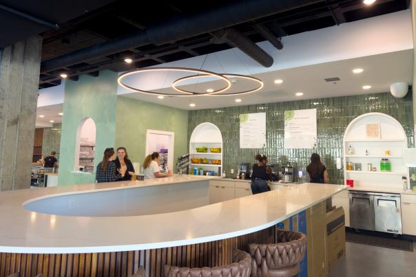 A photo of 3 people at the juice bar in The Society, with 2 baristas behind the bar blending up drinks.