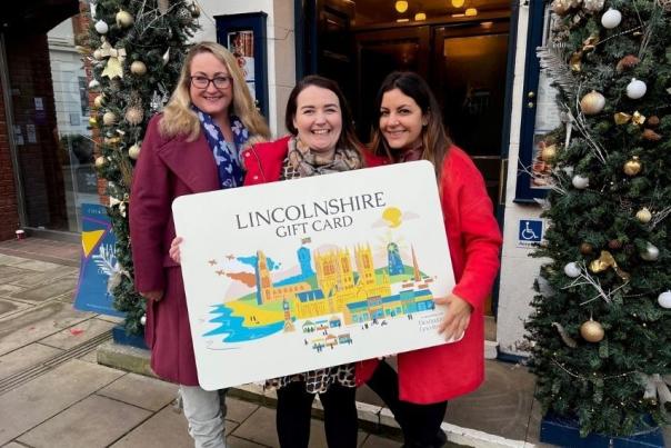 three people holding a giant cut out of the Lincolnshire gift card