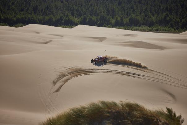 A dune buggy speeds over the Oregon dunes and sand flies up behind it.