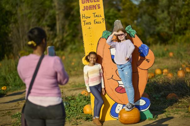 Two girls getting their picture taken in front of a cartoon pumpkin at Uncle John's Cider Mill