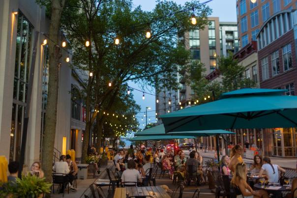 An outdoor patio space in the evening full of people at tables with rows of string lights hanging above them.