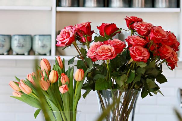 Two vases of flowers, tulips and roses, in front of shelves of merch