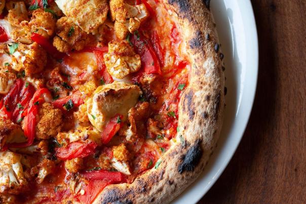 Vegan pizza with red peppers and cauliflower on a white plate on a wood table