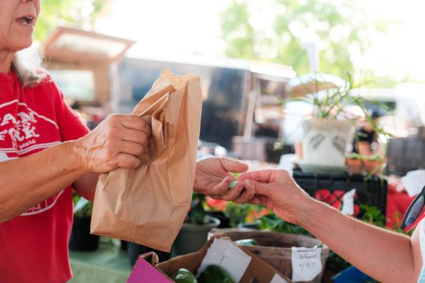Vendor at the Overland Park Farmers' Market hands over a bag to a customer.