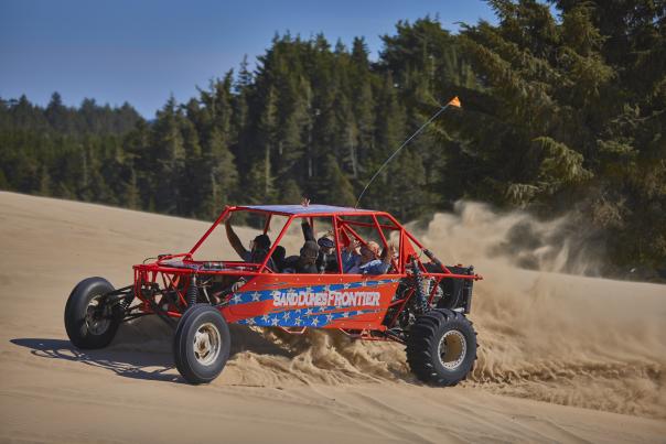A red dune buggy full of smiling people whips up sand on a dune as it spins in a circle.