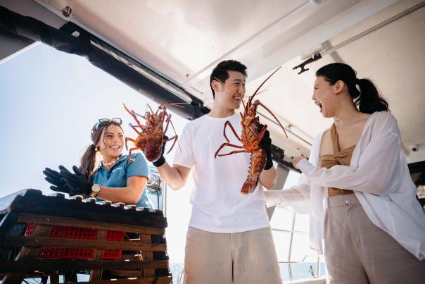 couple holding a lobster pulled out of a lobster pot while on a boat