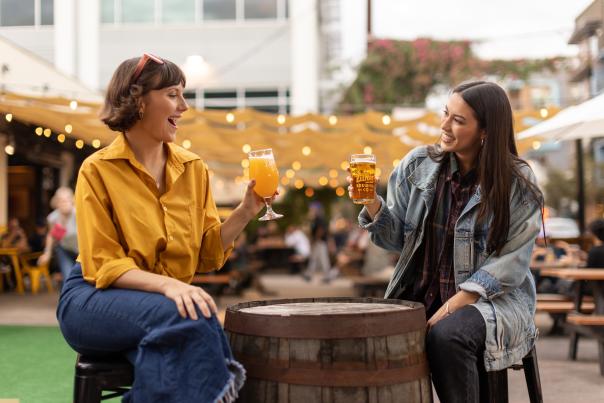 Two women sitting at a bartop at Zilker Brewing Company cheers with glasses of beer