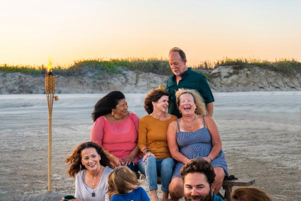 A group of adults sit on the beach, laughing and talking.