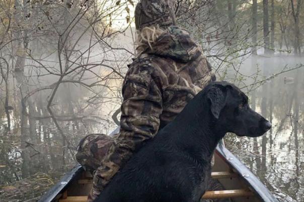 Man duck hunting in boat with black dog