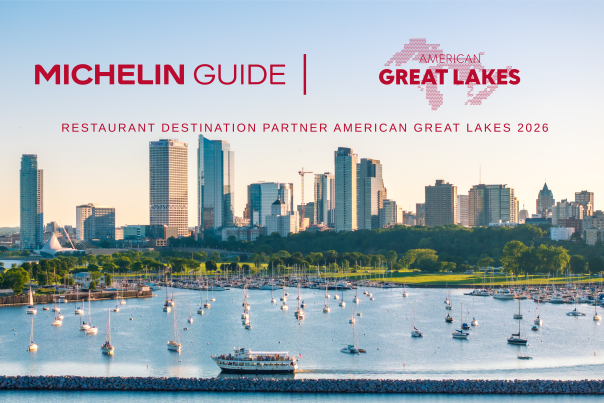 A waterfront view of Milwaukee’s skyline at sunset, with sailboats docked in the marina and a tour boat moving across Lake Michigan in the foreground. Above the skyline, red text reads “Michelin Guide | American Great Lakes” with the subheading “Restaurant Destination Partner American Great Lakes 2026.”