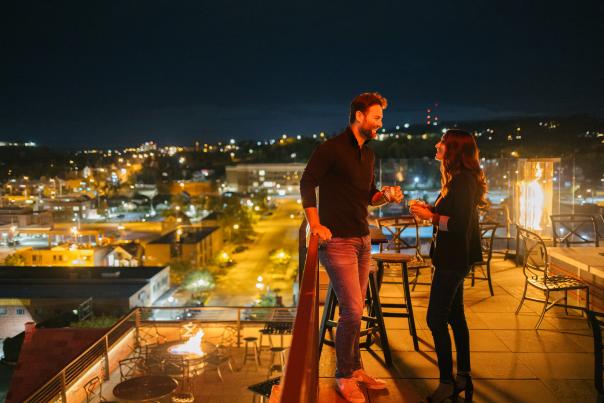 Couple clinking glasses in the evening surround by city lights on the roof of Vertex Sky Bar at Hotel Alex Johnson in Downtown Rapid City, SD
