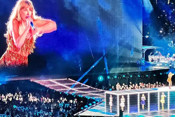 The Taylor Swift eras tour with a full crowd and Taylor on the big screen singing.