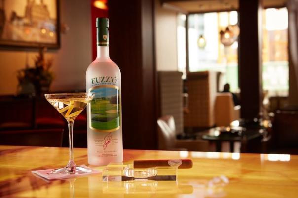 A frosted bottle of Fuzzy's vodka sits atop a light wood counter at BLEND Bar. On its left is a full martini glass with a twist of lemon peel. On its right, a cigar. The lounge area is out of focus behind the counter.