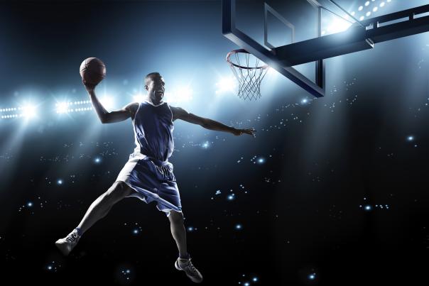 A male basketball player, in the air, ready to dunk the ball