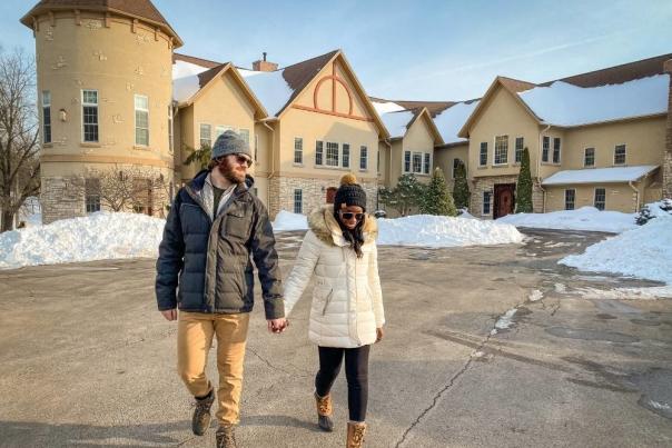 A couple holding hands, standing in front of the Goldmoor Inn, a hotel outside of Galena. They are walking outside in the winter, with snow on the ground.