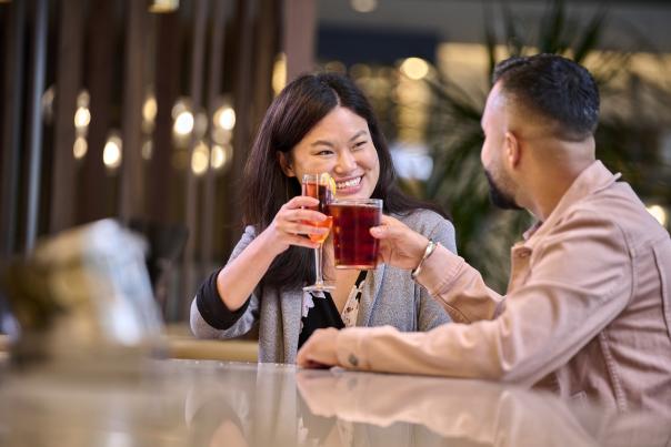 A couple raises their glasses in a toast at Toscana Kitchen & Wine Market's bar, enjoying a memorable night out.