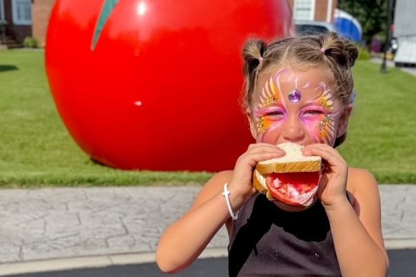 Girl with facepaint eating a tomato sandwich at the Woodleaf Tomato Festival from the Woodleaf Tomato Festival Facebook page