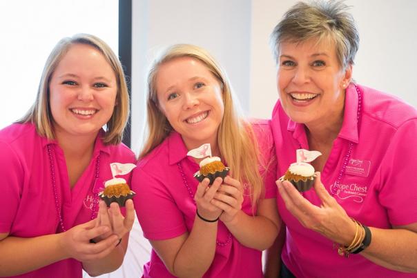 Three women wearing pink and holding cupcakes