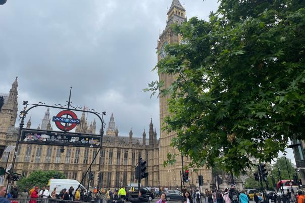 Westminster Station tube sign with Big Ben looming in the background with a tree in the foreground