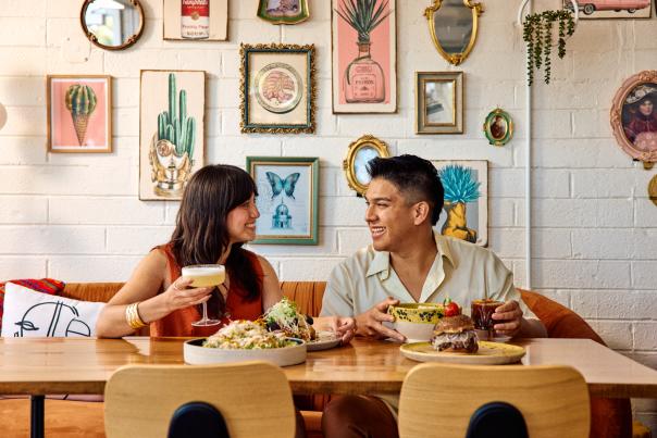 A man and woman sit together at a table in Chilte Restaurant, located in the Grand Ave neighborhood of downtown Phoenix. Plates of food are in front of them, and the wall behind them is covered in framed artwork.