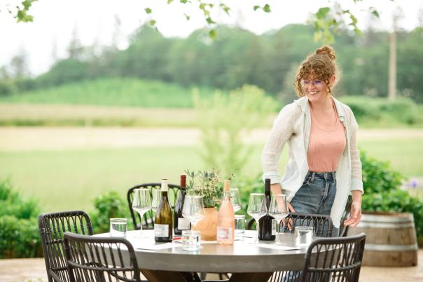 A woman looks at a table set for wine tasting with glasses and wine bottles.