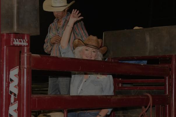 A lady is on a bull waving her arm and ready to compete at the Estes Field PCA Rodeo