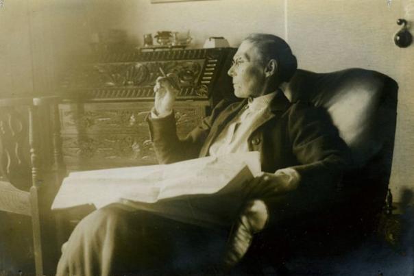 Sepia photo of Amy Dilllwyn sitting in chair reading a paper.