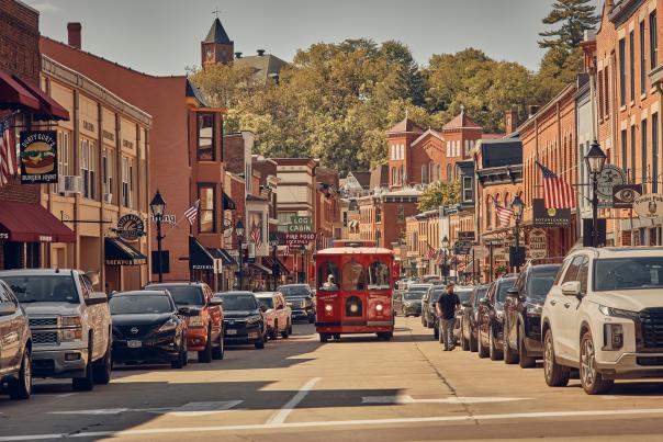 Image of downtown Galena, on its Main Street. Photo includes a red trolley bus driving on the street with red brick buildings on both sides.
