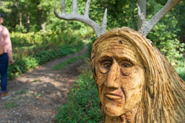 A statue of a woman's face welcomes hikers along a wooded path at The Farley Center.