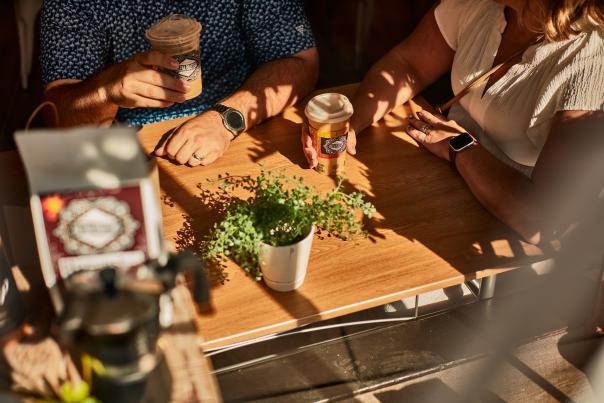 Two people sitting at a table in the sunlight, drinking coffees.