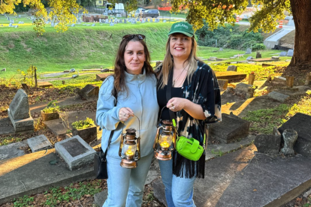 Two women stand in a graveyard holding lanterns