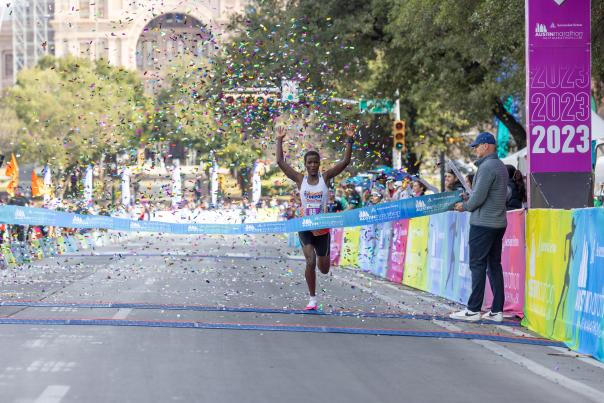 Image of a man crossing the finish line with his hands in the air at the Austin Marathon.