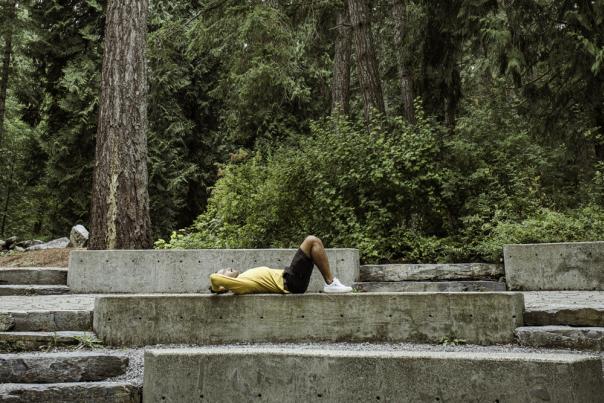 Person lying on a concrete bench in a forested park.