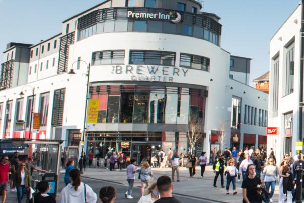 A busy street scene showing the entrance to the Brewery Quarter with lots of shoppers