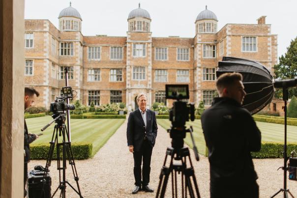 A man being interviewed on camera, stood infront of Doddington Hall