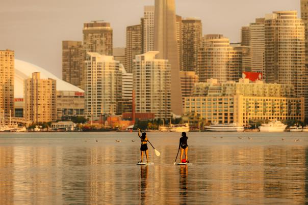 Two people on paddle boards on Lake Ontario, with the Toronto skyline in the background.