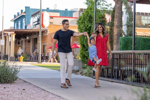 Mother and father swinging little girl between them walking down the sidewalk in Downtown Chandler.